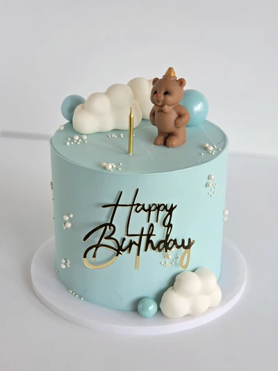 Pastel blue teddy bear birthday cake with clouds and gold topper