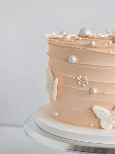 Blush buttercream cake with pearl details and white butterflies