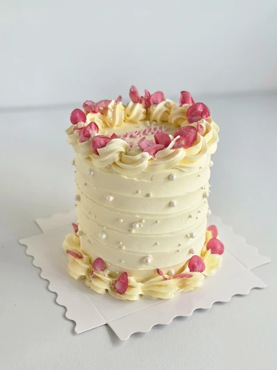 Custom ivory buttercream cake with pink petals and pearl details