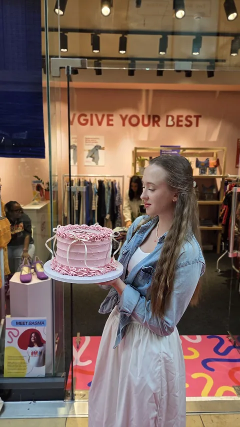 Marharyta Makus holding a pink cake outside the Give Your Best shop at Grand Arcade Cambridge