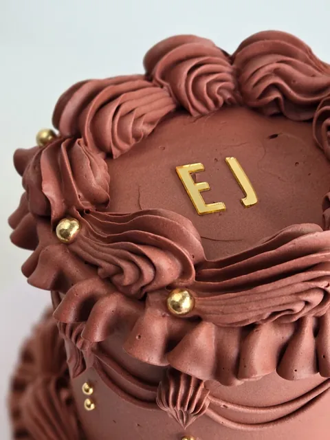Close-up of chocolate celebration cake with vintage piping, gold pearls and monogram topper