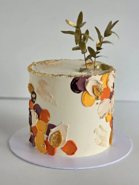 Tall ivory celebration cake with autumn buttercream accents, gold leaf and foliage