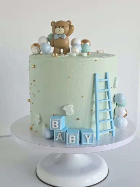 Pale blue baby celebration cake with teddy bear, BABY blocks, ladder and balloons