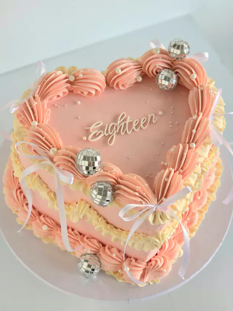 Pink heart-shaped eighteenth birthday cake with disco balls, pearls and ribbon bows