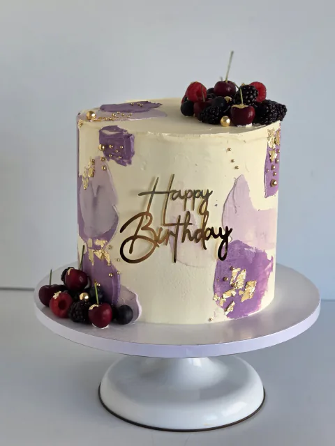 Ivory and purple celebration cake with cherries, berries and gold leaf