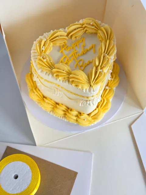 Yellow and cream heart-shaped birthday cake with vintage piping in a gift box