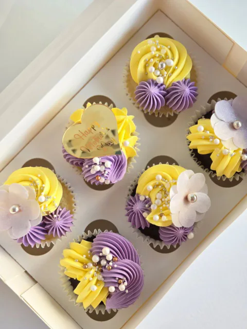 Purple and yellow floral cupcakes arranged in a gift box