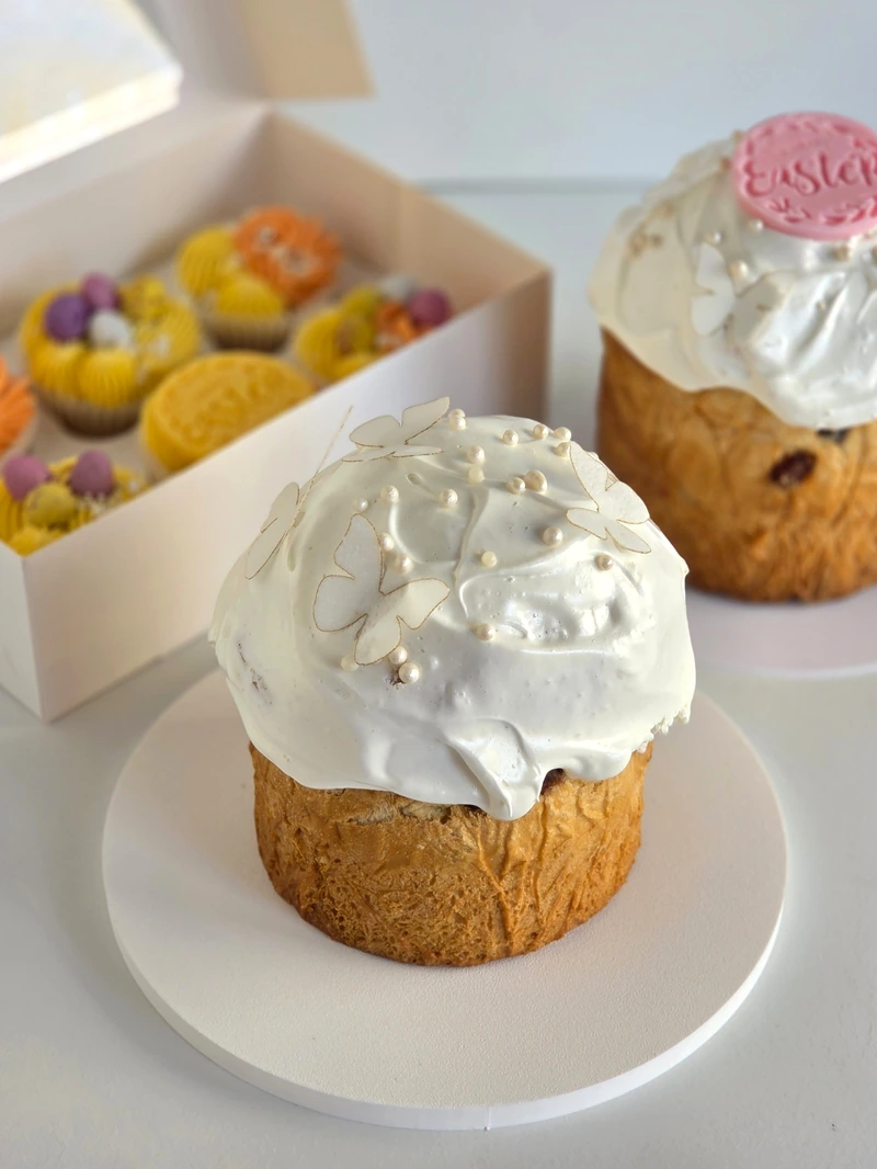 Traditional Easter Paska with white meringue icing and spring cupcakes in the background