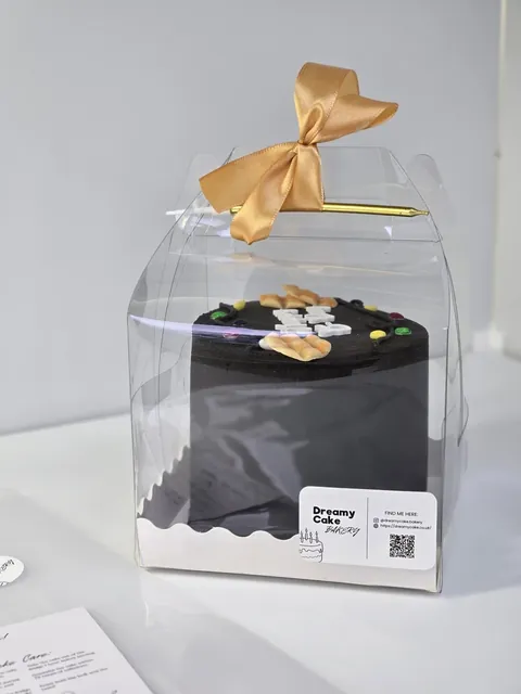 Black mini bento cake packaged in a clear gift box with a gold satin bow