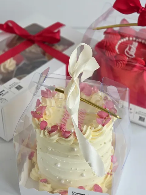 Mini bento cake in a clear gift box with white ribbon and gift boxes in the background