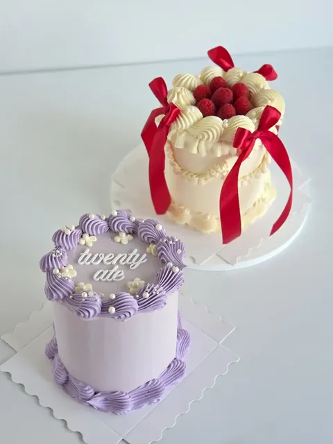 Lilac vintage buttercream cake with piped swags and lettering, with ribbon cake in the background