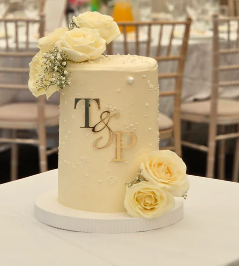 White wedding cake with fresh roses and gold initials in a wide venue setting