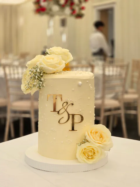 White wedding cake with fresh roses, baby's breath and gold T and P initials at the venue