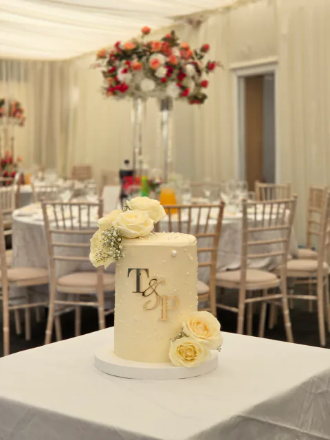 White wedding cake with fresh roses and gold initials in a wide venue setting
